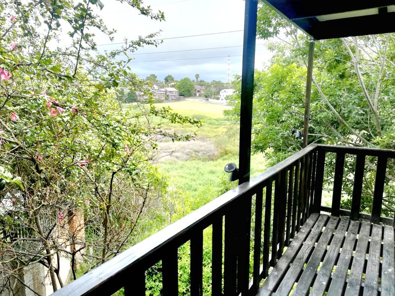 An elevated timber balcony featuring a wooden balustrade and decking, offering an open view of the surrounding greenery and neighborhood.