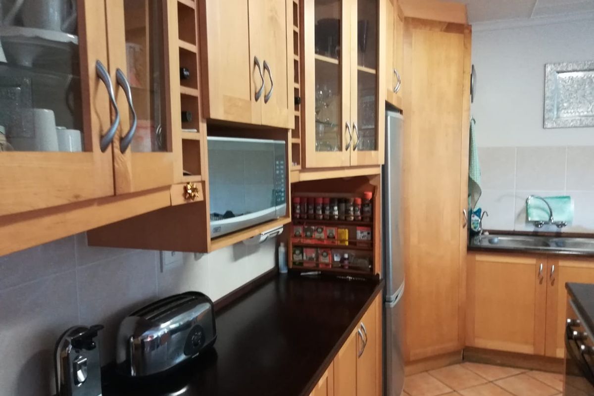 A functional kitchen featuring wooden cabinetry, dark laminate countertops, built-in microwave, and tiled flooring with a stainless steel sink area.