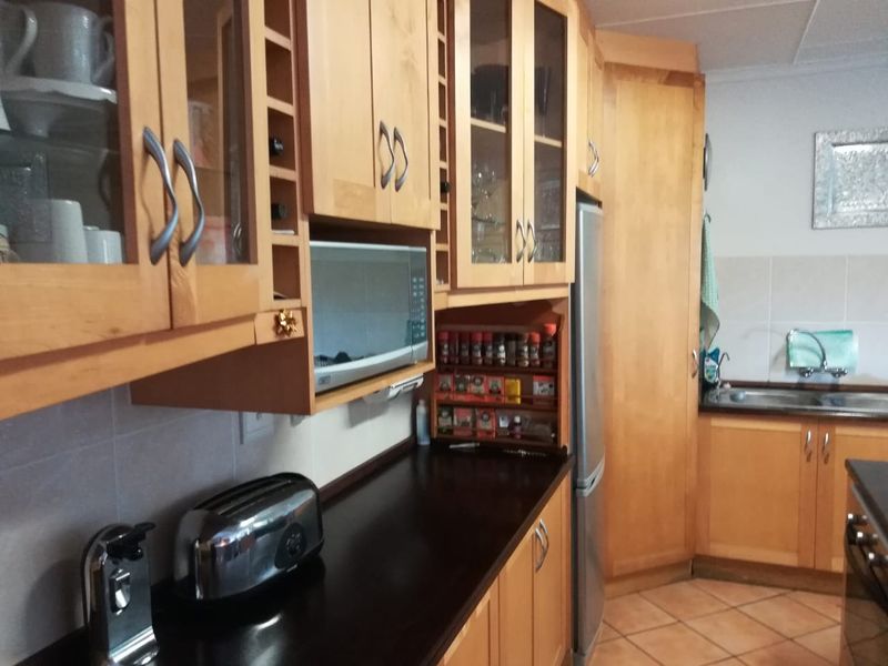 A functional kitchen featuring wooden cabinetry, dark laminate countertops, built-in microwave, and tiled flooring with a stainless steel sink area.