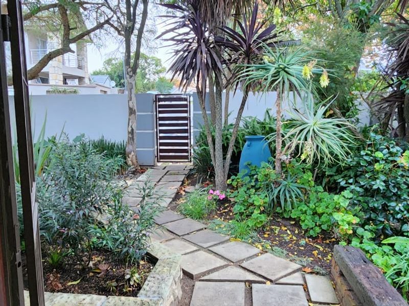 A well-maintained private garden featuring stone paved pathways, established greenery, and a secure boundary wall with a pedestrian gate.