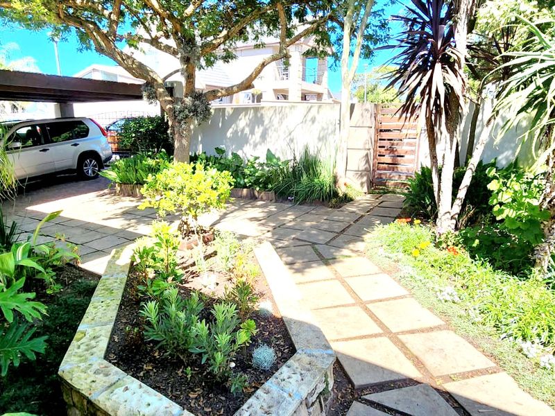 A landscaped front garden area featuring a paved driveway, a covered carport, and a raised stone garden bed.