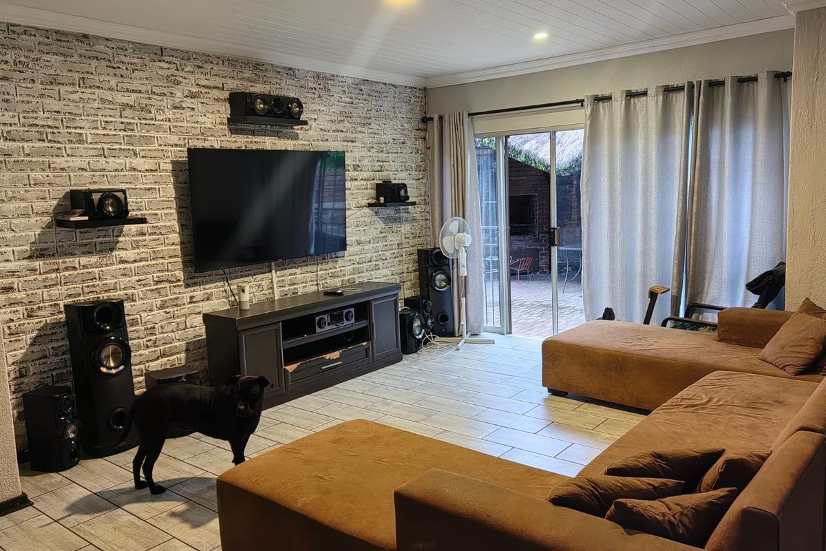 A comfortable living room featuring an exposed brick accent wall, tiled flooring, and direct access to an outdoor patio through sliding glass doors.