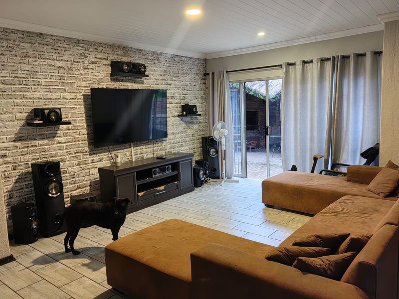 A comfortable living room featuring an exposed brick accent wall, tiled flooring, and direct access to an outdoor patio through sliding glass doors.