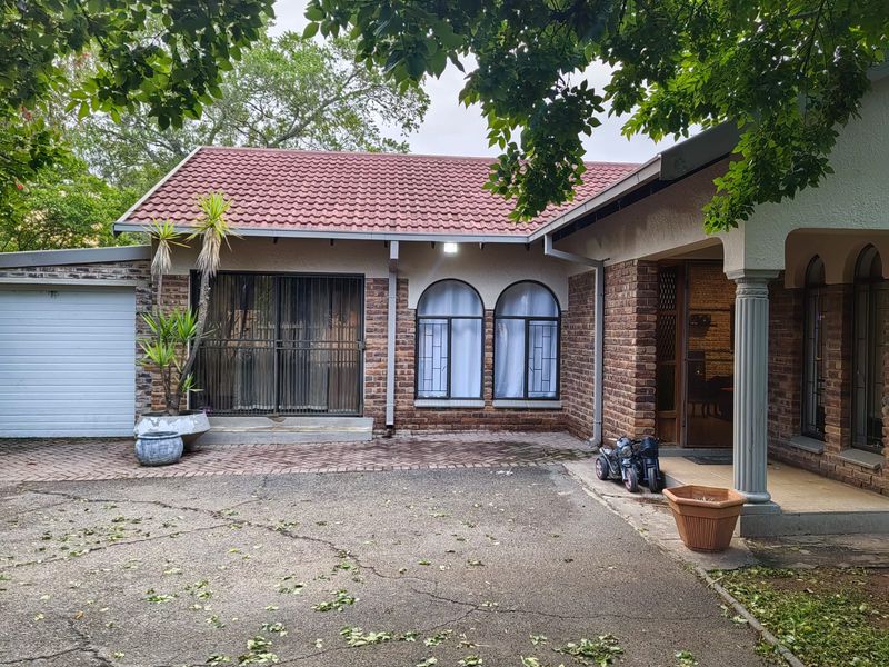 Front elevation of a single-story brick house featuring a tiled roof, arched windows, security gates, and an attached garage with a paved driveway.
