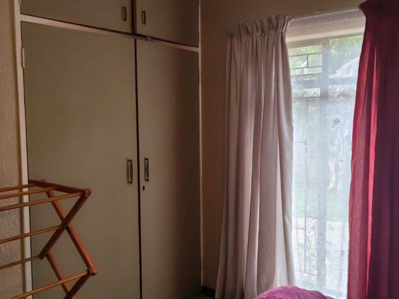 A bedroom featuring built-in cupboards, tiled flooring, and a window fitted with security bars.