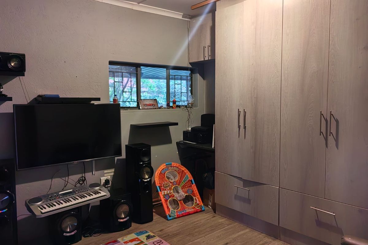 A bedroom featuring built-in cupboards, laminate flooring, and a window with security bars.