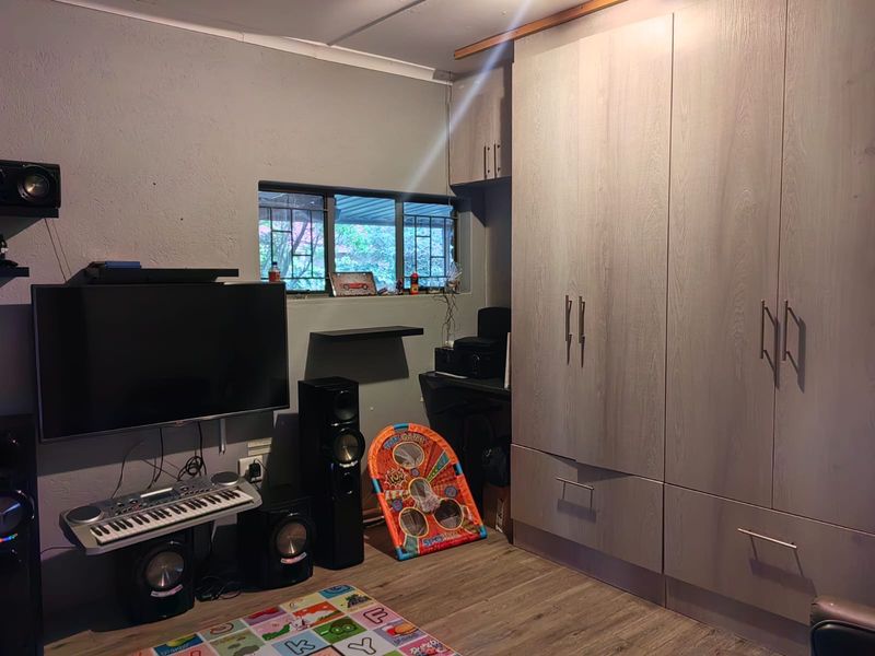 A bedroom featuring built-in cupboards, laminate flooring, and a window with security bars.