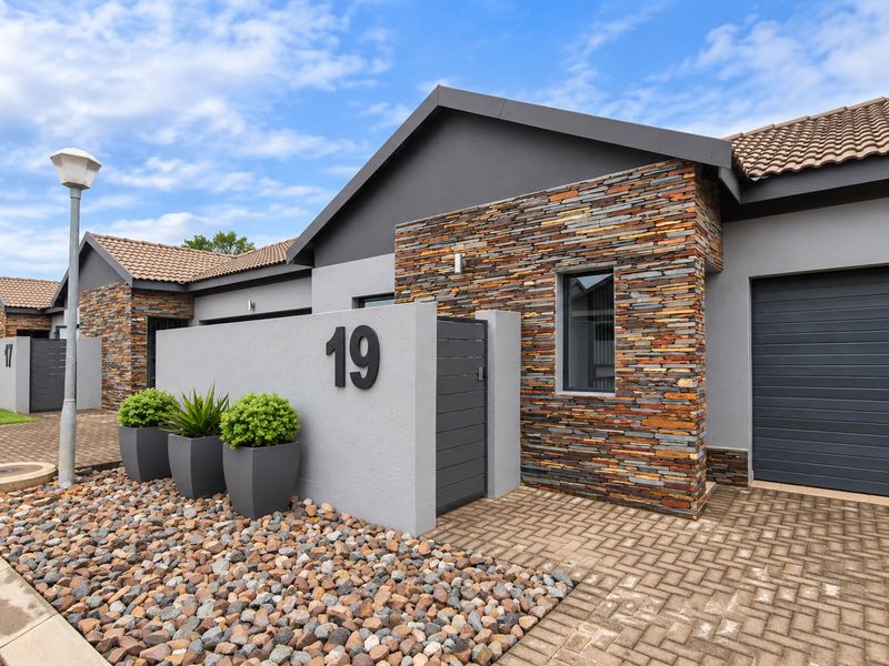 Modern front facade featuring stone cladding, a paved driveway, and a secure garage entrance with a contemporary design.