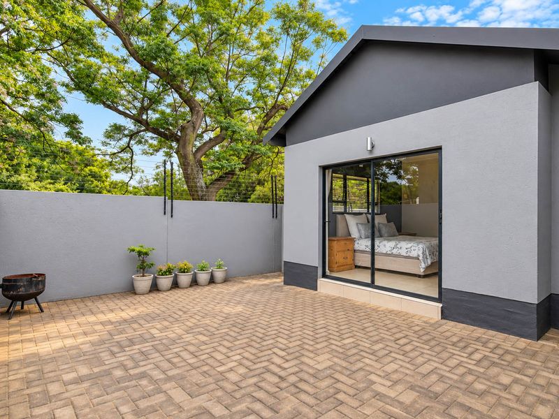 A well-maintained rear exterior featuring a paved patio area, sliding glass door access to the bedroom, and secure perimeter walling with electric fencing.