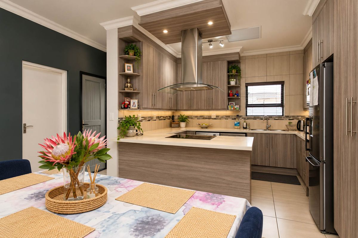 Modern kitchen featuring wood-grain cabinetry, stone countertops, integrated hob, stainless steel extractor fan, and tiled backsplash with under-cabinet lighting.
