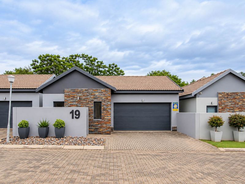Modern front facade featuring a paved driveway, stone-clad accents, and an automated garage door, presenting a well-maintained and contemporary street appeal.