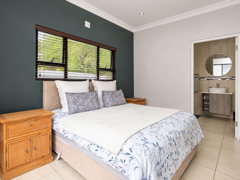 A well-maintained bedroom featuring tiled floors, a dark accent wall, and an adjoining en-suite bathroom with a modern vanity.