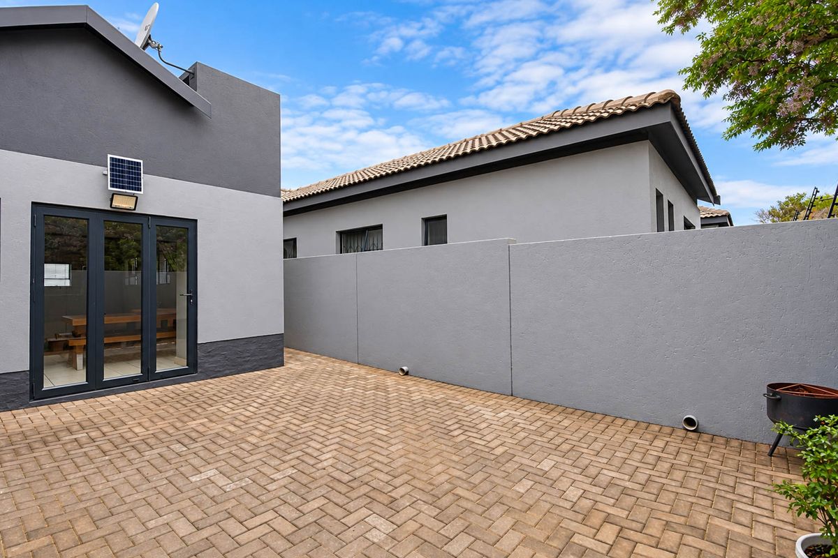 A well-maintained rear courtyard featuring paved flooring, a high boundary wall for privacy, and modern glass doors leading into the home.