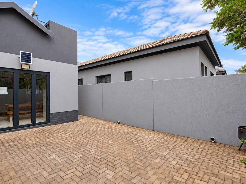 A well-maintained rear courtyard featuring paved flooring, a high boundary wall for privacy, and modern glass doors leading into the home.