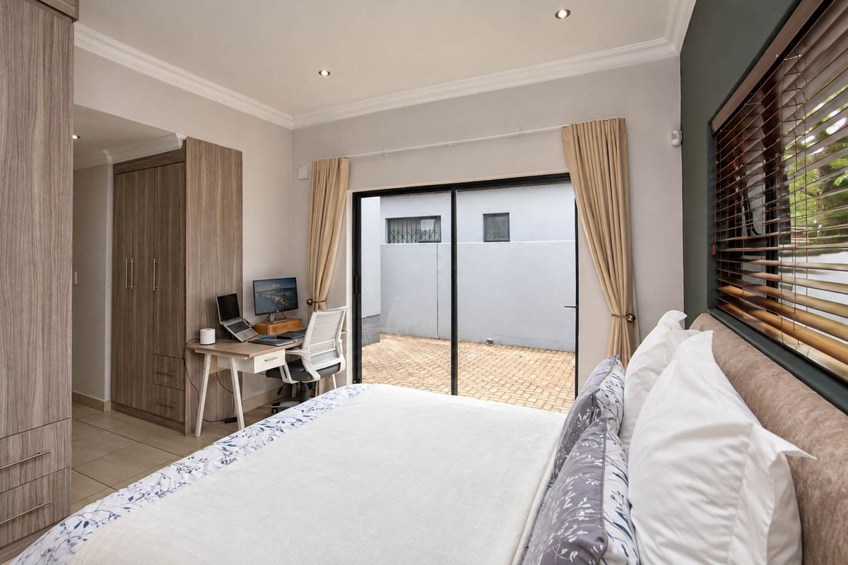 A well-maintained bedroom featuring built-in cupboards, tiled flooring, recessed lighting, and a sliding glass door providing direct access to an outdoor paved area.