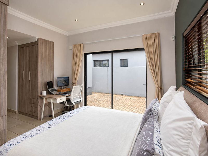 A well-maintained bedroom featuring built-in cupboards, tiled flooring, recessed lighting, and a sliding glass door providing direct access to an outdoor paved area.