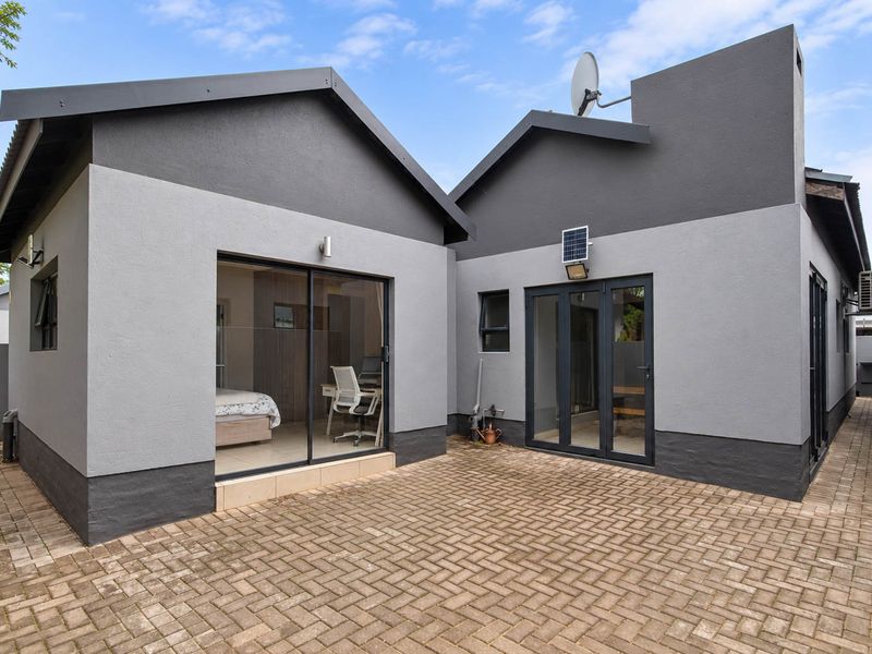 A modern rear courtyard featuring paved flooring, dual-tone exterior walls, and access to the home via sliding and french doors.