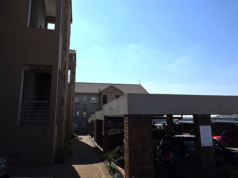 Exterior view of the apartment complex featuring a paved walkway and covered parking bays with brick pillar supports.