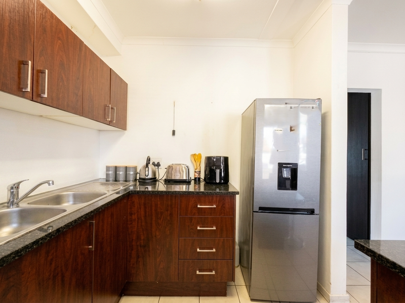 A functional kitchen featuring dark wood-look cabinetry, granite countertops, and a stainless steel double sink with tiled flooring.