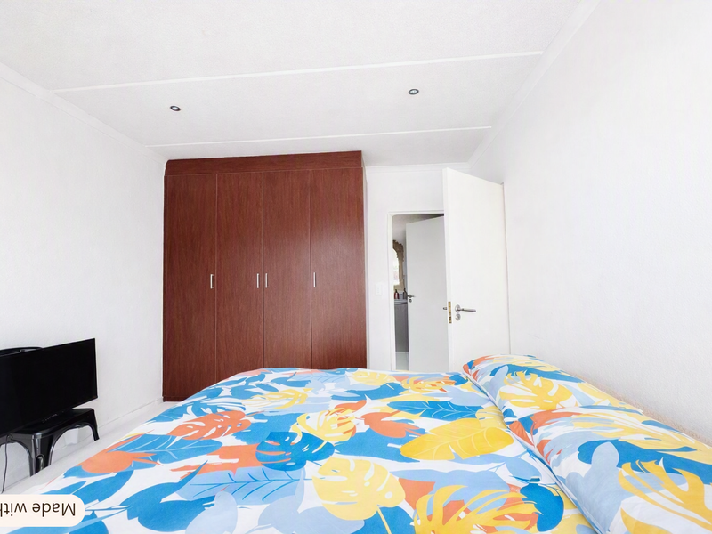 A bedroom featuring built-in wooden cupboards and recessed ceiling lighting, with a doorway leading to an adjacent room.