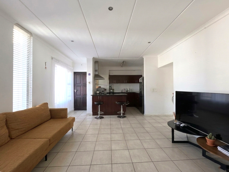 Open-plan living area featuring tiled flooring, a kitchen with dark cabinetry and an island, and large windows with venetian blinds.