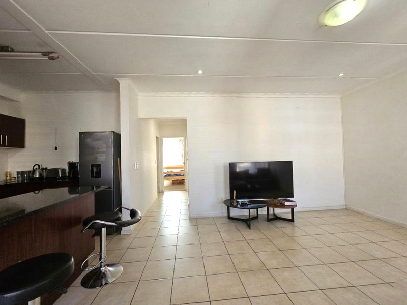 Open plan living area featuring tiled flooring and a kitchen with dark cabinetry and granite countertops, leading to a hallway.
