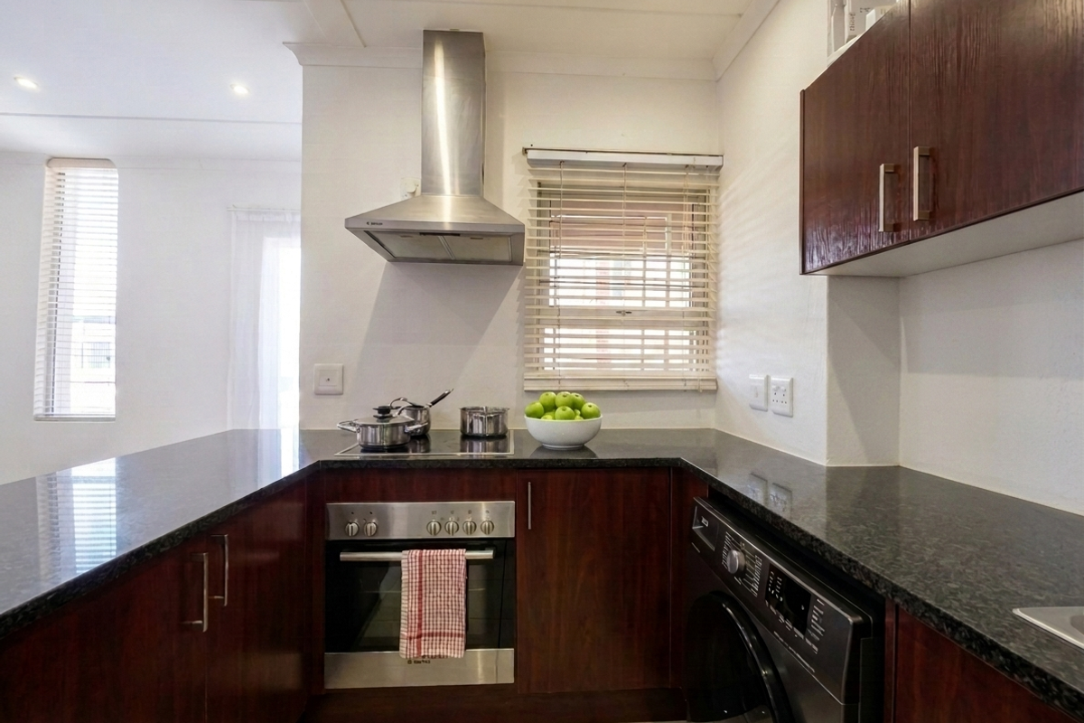 A well-maintained kitchen featuring dark wood cabinetry, granite countertops, a stainless steel extractor fan, and a built-in oven with an electric hob.