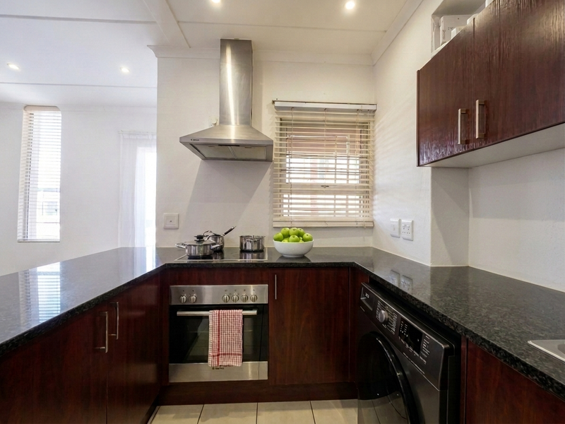 A well-maintained kitchen featuring dark wood cabinetry, granite countertops, a stainless steel extractor fan, and a built-in oven with an electric hob.