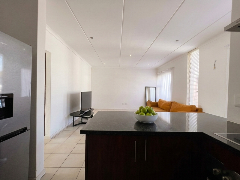 Open plan living area featuring a kitchen with dark wood cabinetry and granite countertops, flowing into a tiled lounge space with natural light.