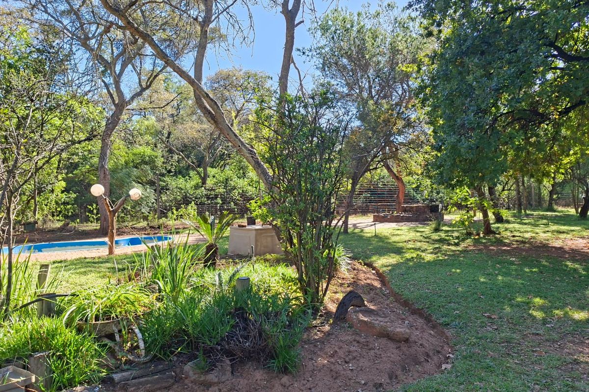 A spacious, tree-filled garden area featuring a swimming pool, established landscaping, and perimeter fencing, offering a natural and private outdoor setting.