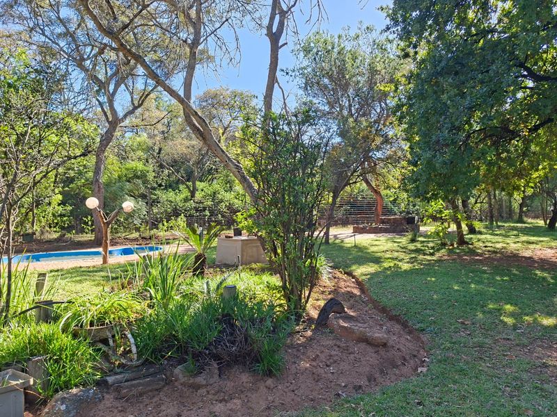 A spacious, tree-filled garden area featuring a swimming pool, established landscaping, and perimeter fencing, offering a natural and private outdoor setting.