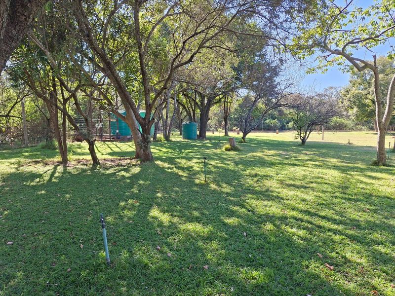 A spacious, well-established garden area featuring mature trees, open lawn space, and functional water storage tanks on the property.