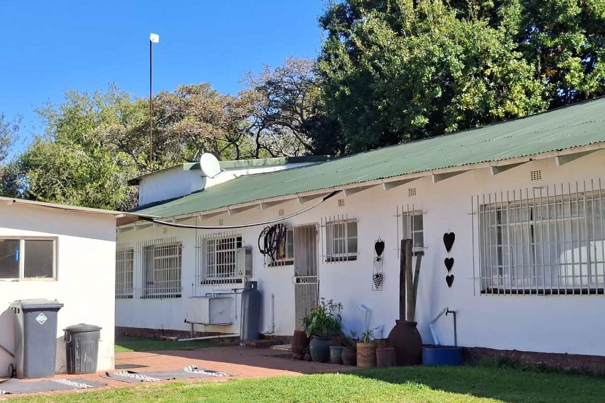 Rear view of the property showing a single-story structure with a green corrugated metal roof, security bars on windows, and a paved patio area.