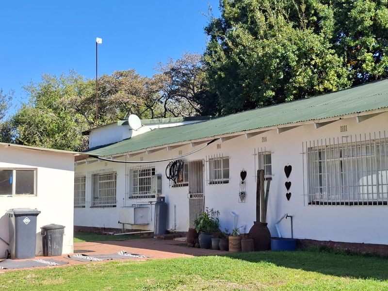 Rear view of the property showing a single-story structure with a green corrugated metal roof, security bars on windows, and a paved patio area.