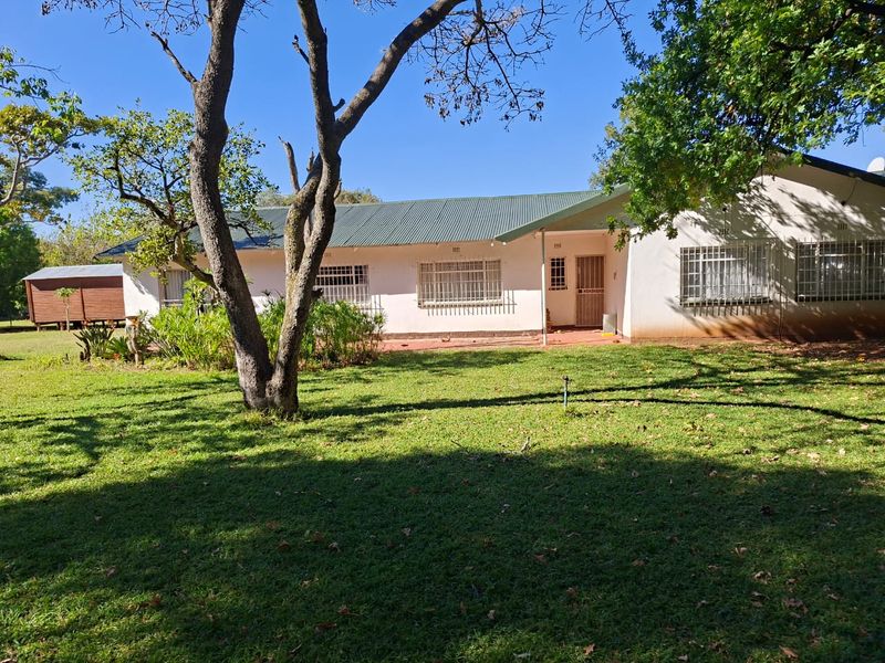 A view of the rear elevation of the house featuring a corrugated metal roof, security bars on windows, and a spacious garden area.