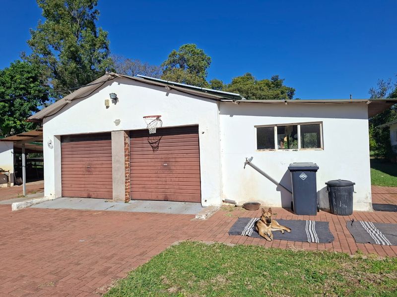 A detached double garage with brick paving and exterior wall-mounted lighting, showing signs of wear on the facade and garage doors.