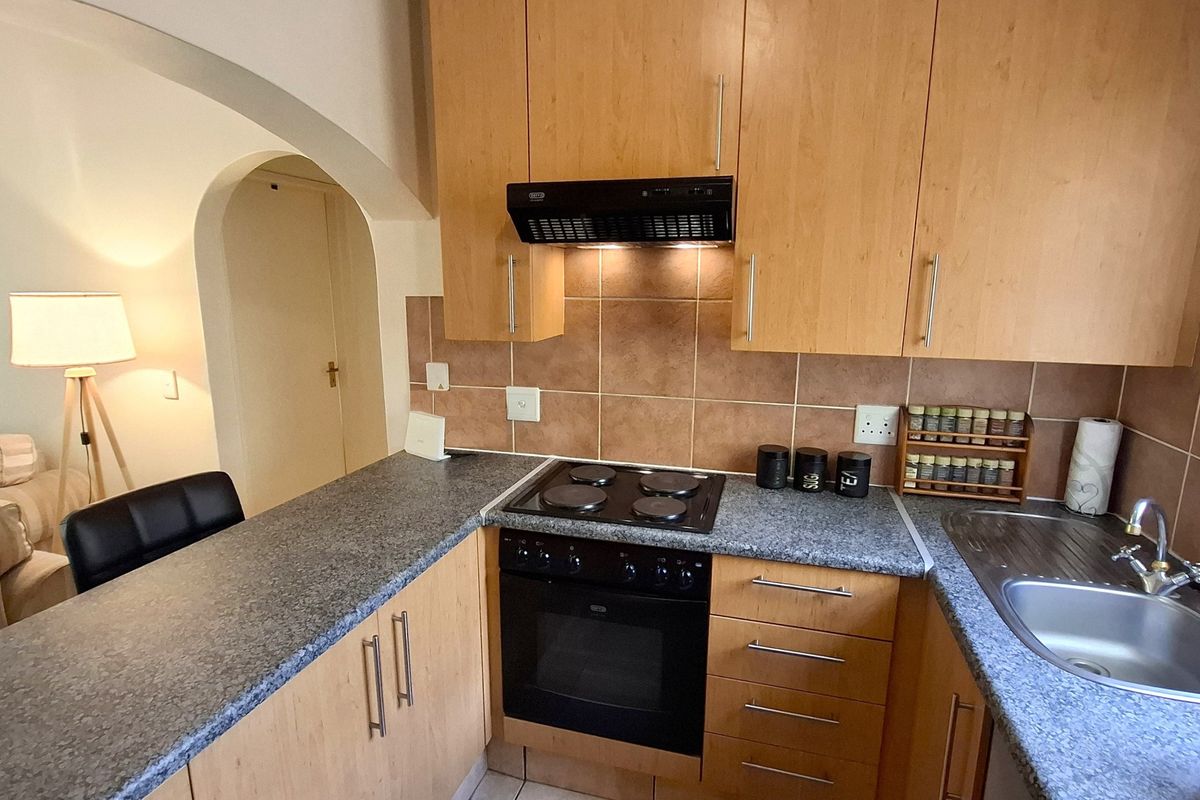 A functional kitchen featuring light wood-finish cabinetry, granite-look laminate countertops, a built-in electric oven and hob, and a tiled backsplash.