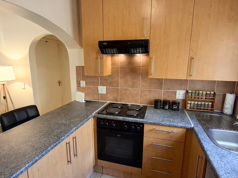 A functional kitchen featuring light wood-finish cabinetry, granite-look laminate countertops, a built-in electric oven and hob, and a tiled backsplash.