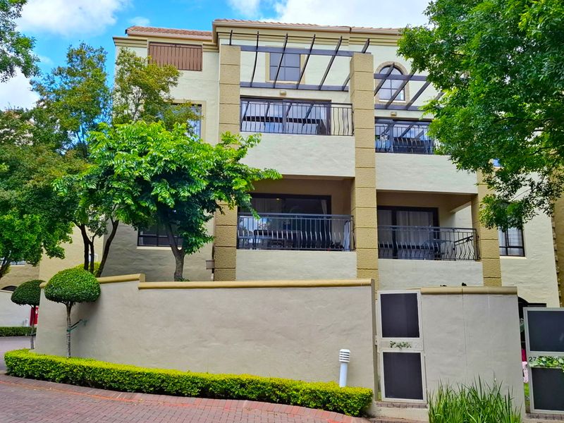 Front elevation of a multi-story apartment complex featuring balconies, a pergola, and a well-maintained boundary wall with landscaped garden elements.