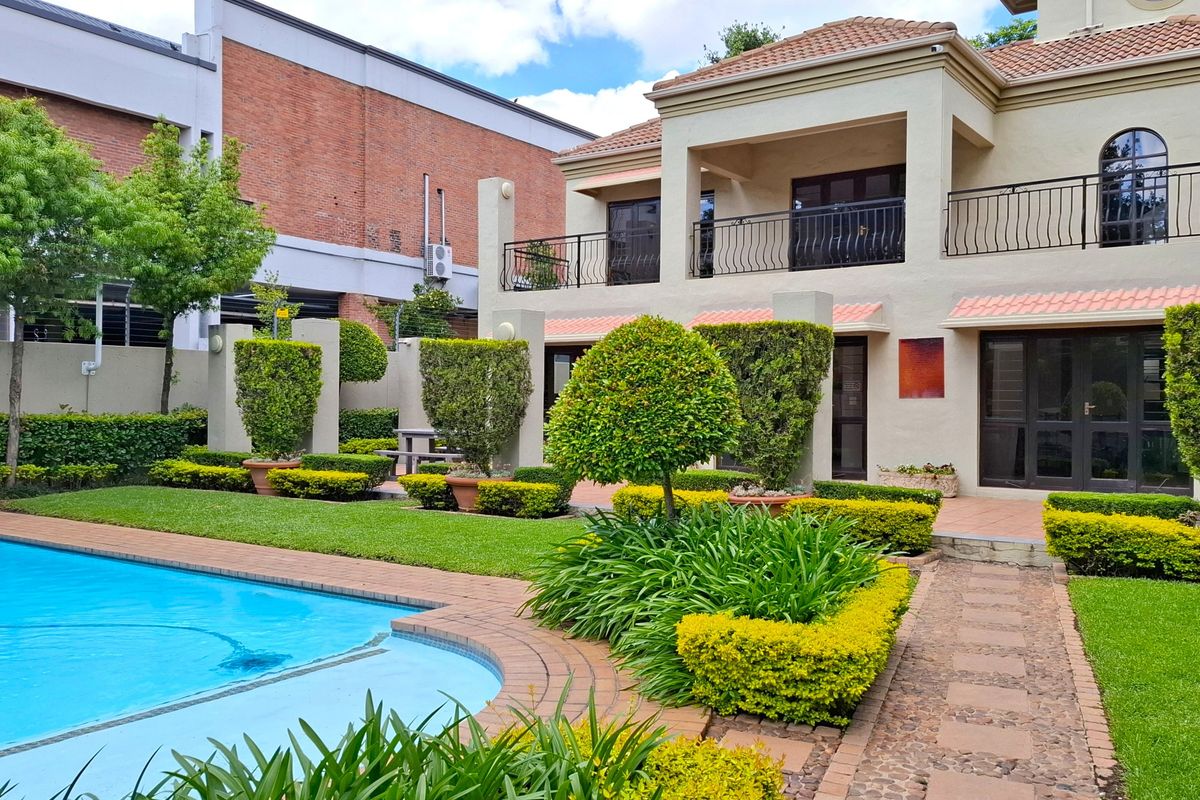 Rear view of the property featuring a well-maintained swimming pool, landscaped garden, paved pathways, and a covered balcony with wrought iron railings.