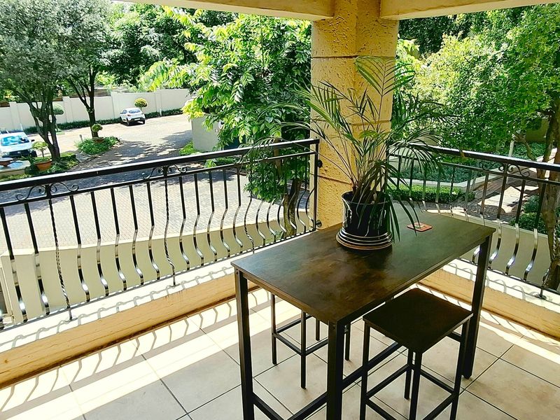 A covered balcony featuring tiled flooring and a decorative wrought iron balustrade, overlooking the complex grounds and parking area.