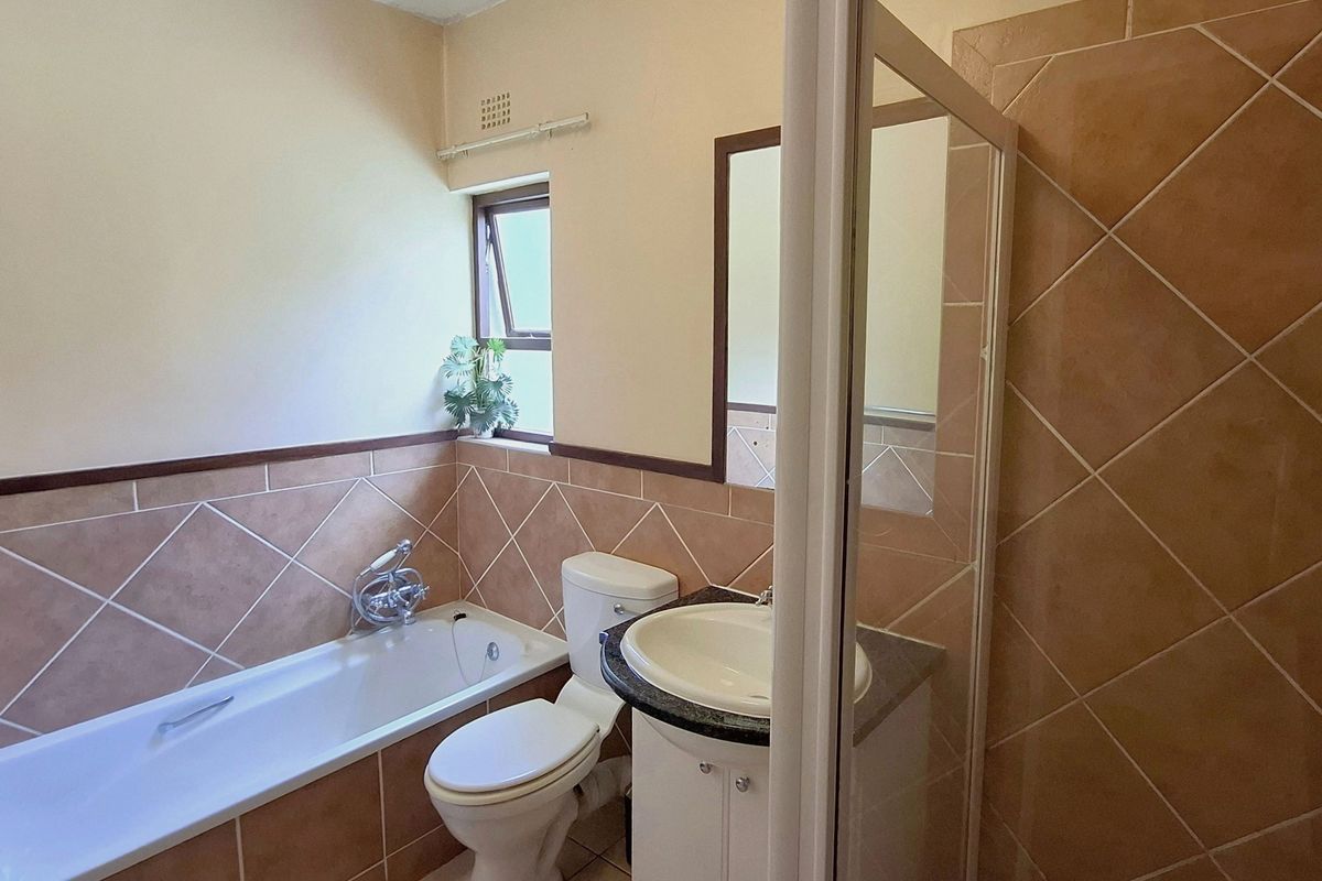 A functional bathroom featuring a bathtub, toilet, and vanity cabinet with a basin, finished with neutral wall tiles.