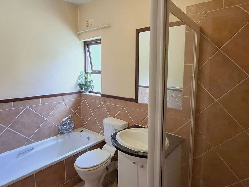 A functional bathroom featuring a bathtub, toilet, and vanity cabinet with a basin, finished with neutral wall tiles.