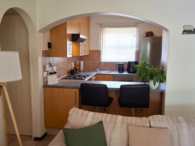 Open plan kitchen featuring light wood cabinetry, laminate countertops, and a breakfast bar, viewed through a decorative arched opening from the living area.