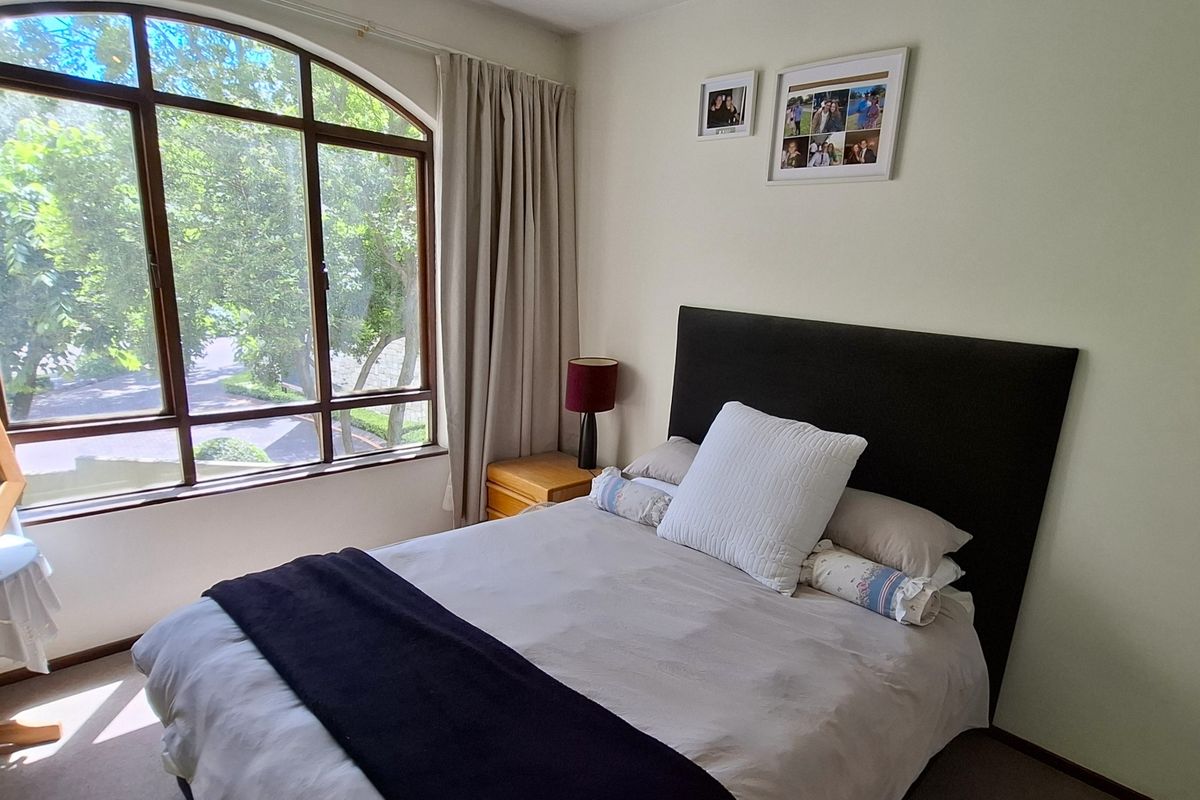A well-lit bedroom featuring a large arched window with views, neutral wall finishes, and carpeted flooring.