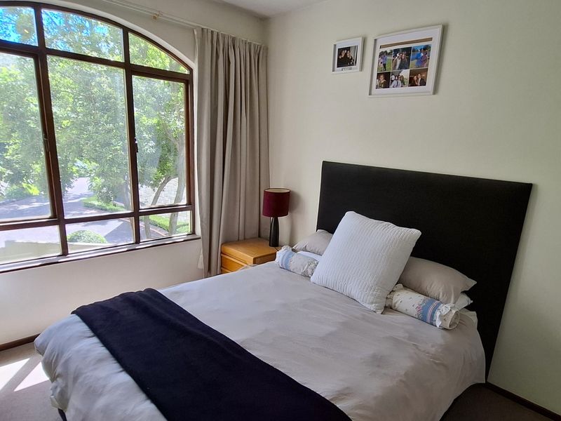 A well-lit bedroom featuring a large arched window with views, neutral wall finishes, and carpeted flooring.
