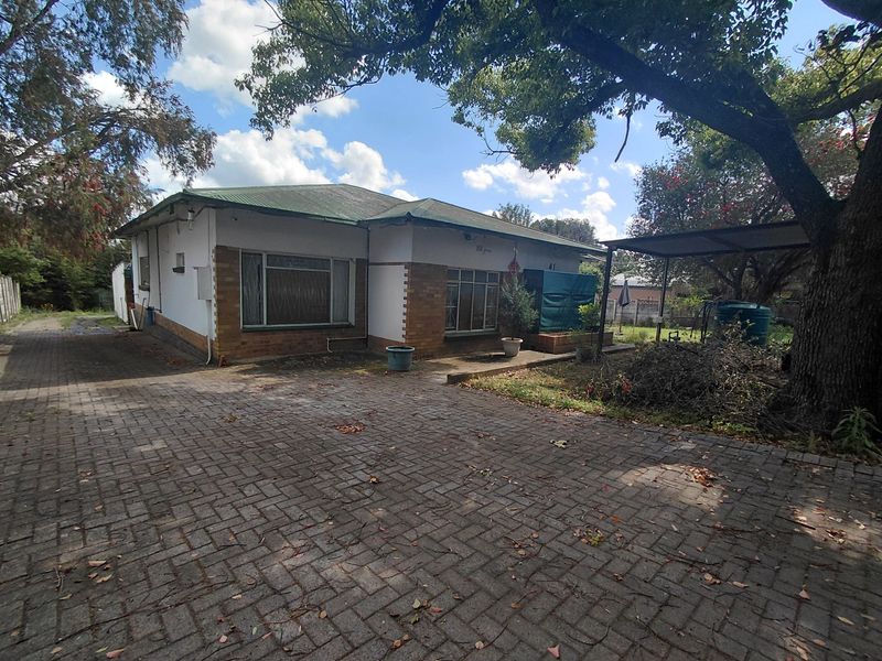 Front view of a single-story house featuring a paved driveway, carport, and brick and plaster facade with a corrugated metal roof.