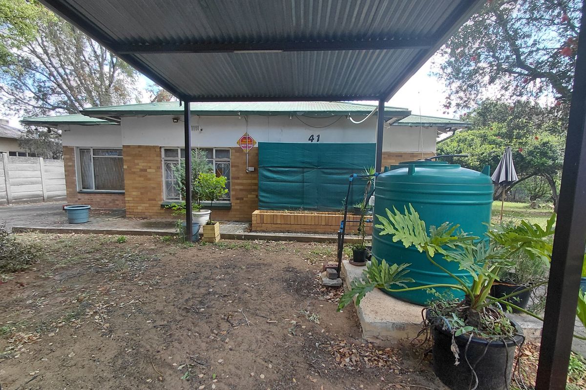 Rear view of the property featuring a corrugated metal carport, brick planter box, and a water storage tank on a concrete base.