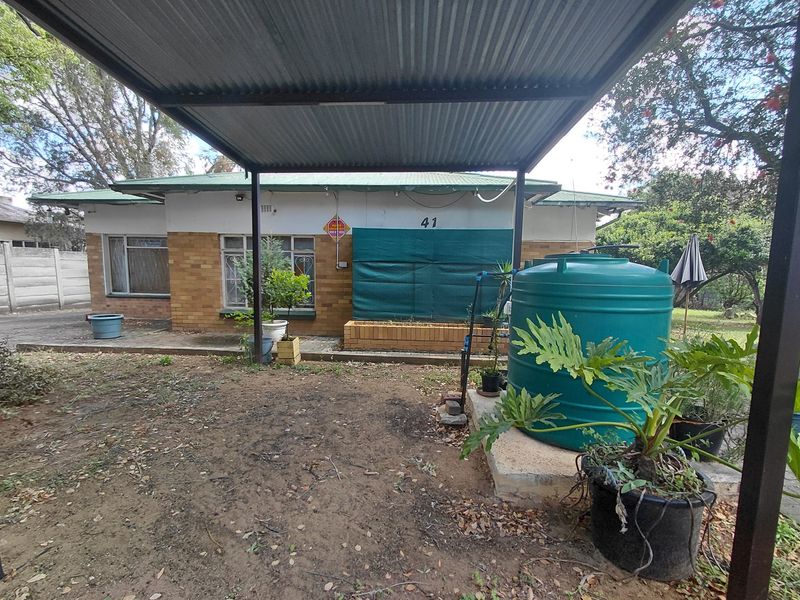 Rear view of the property featuring a corrugated metal carport, brick planter box, and a water storage tank on a concrete base.