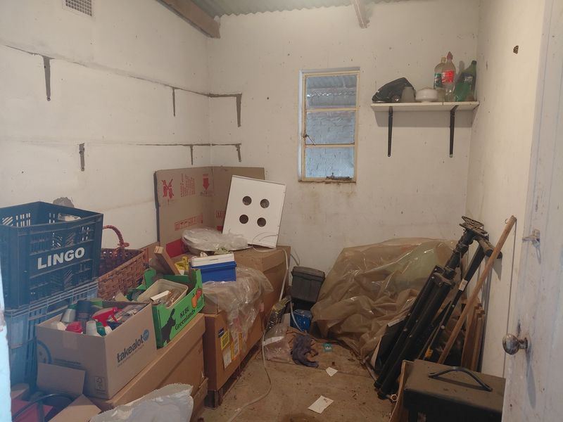 A small utility or storage space featuring exposed masonry walls, a steel-framed window, and unfinished flooring, suitable for renovation or improved storage organization.